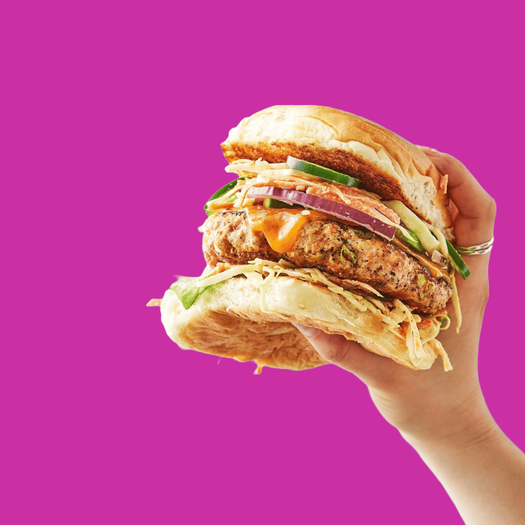 Change management burger recipe 2 – Establish A hand holding a layered burger on a pink backgroun