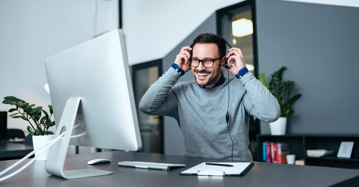 m365-how-do-i-featured A man in business casual clothing smiles and puts on a headset to take a call
