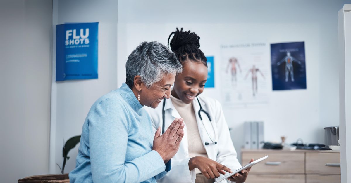 A GP sits beside an elderly patient. She shares information on a tablet screen.