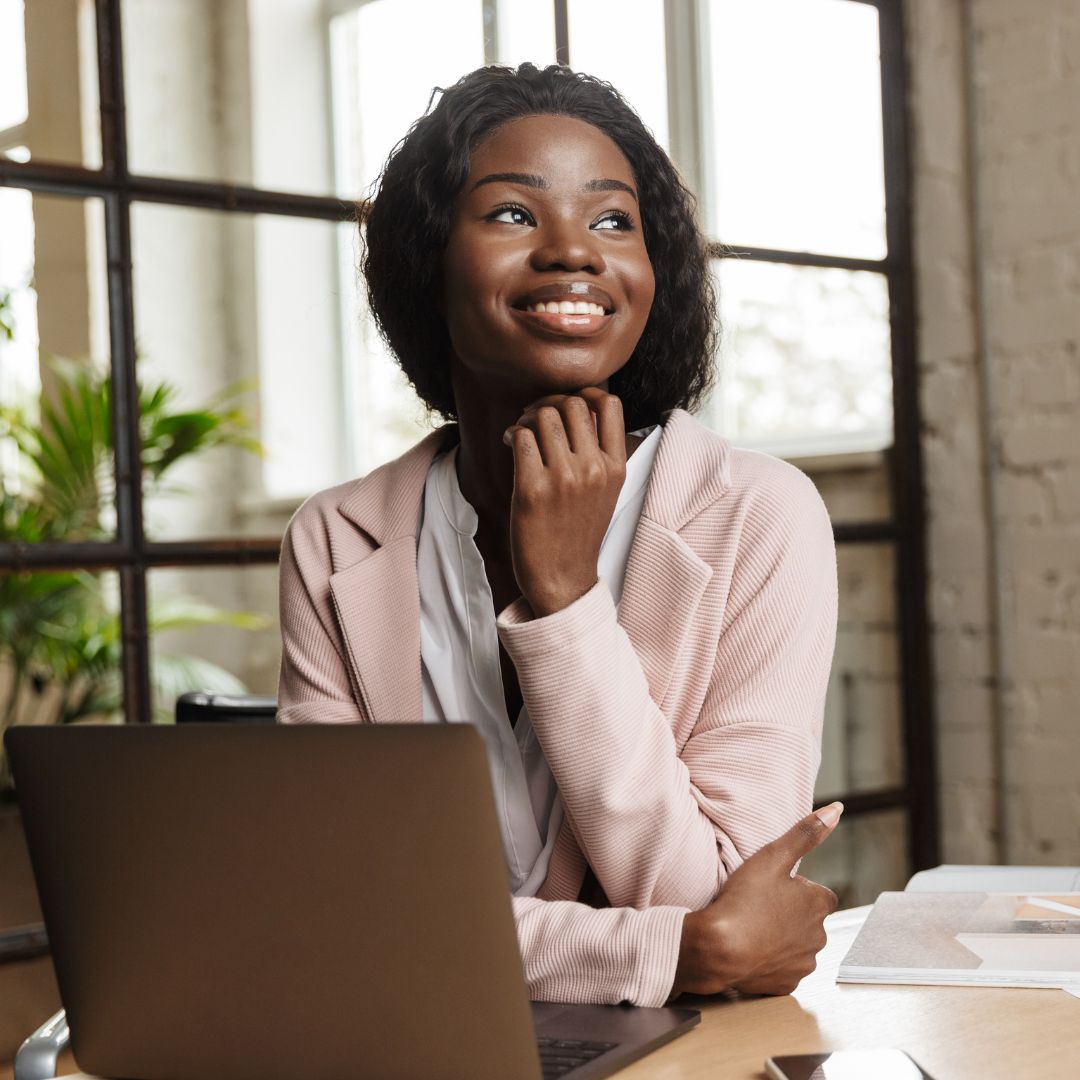 digital-fluency-confidence-with-technology A woman sits in an office in front of her laptop. She radiates confidence and is smiling.