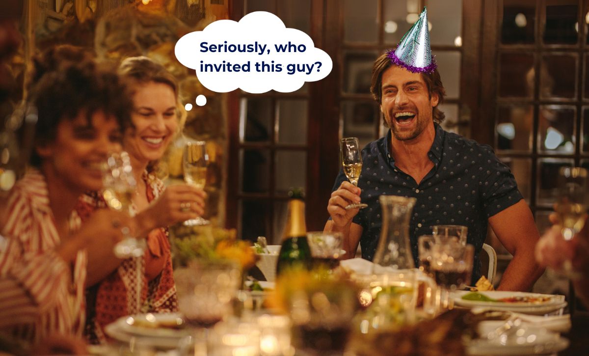 An obnoxious man wearing a party hat sits at a dinner table, eating and drinking. Two women sit to the side smiling awkwardly. A thought bubble emerges from one of the women, it says "seriously, who invited this guy?"